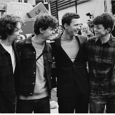 Tom Holland in the middle wearing a suit laughs around his three brothers